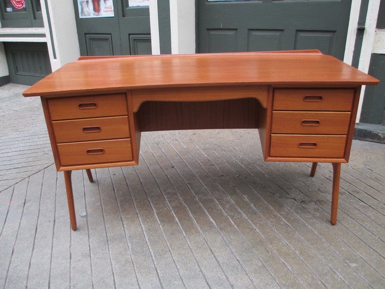 Curved desk with two banks of three drawers each supported by two arched U shaped legs .  Large book shelf spans the entire front of desk.  Surface of desk has a pencil saver curved lip.  Executive desk suitable for home use.  Each drawer has burnt